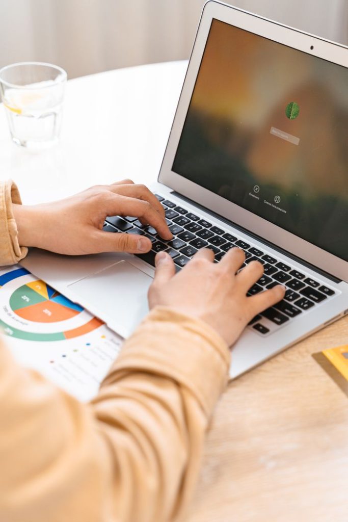 Close-up of hands typing on a laptop with charts visible, suggesting data analysis work.